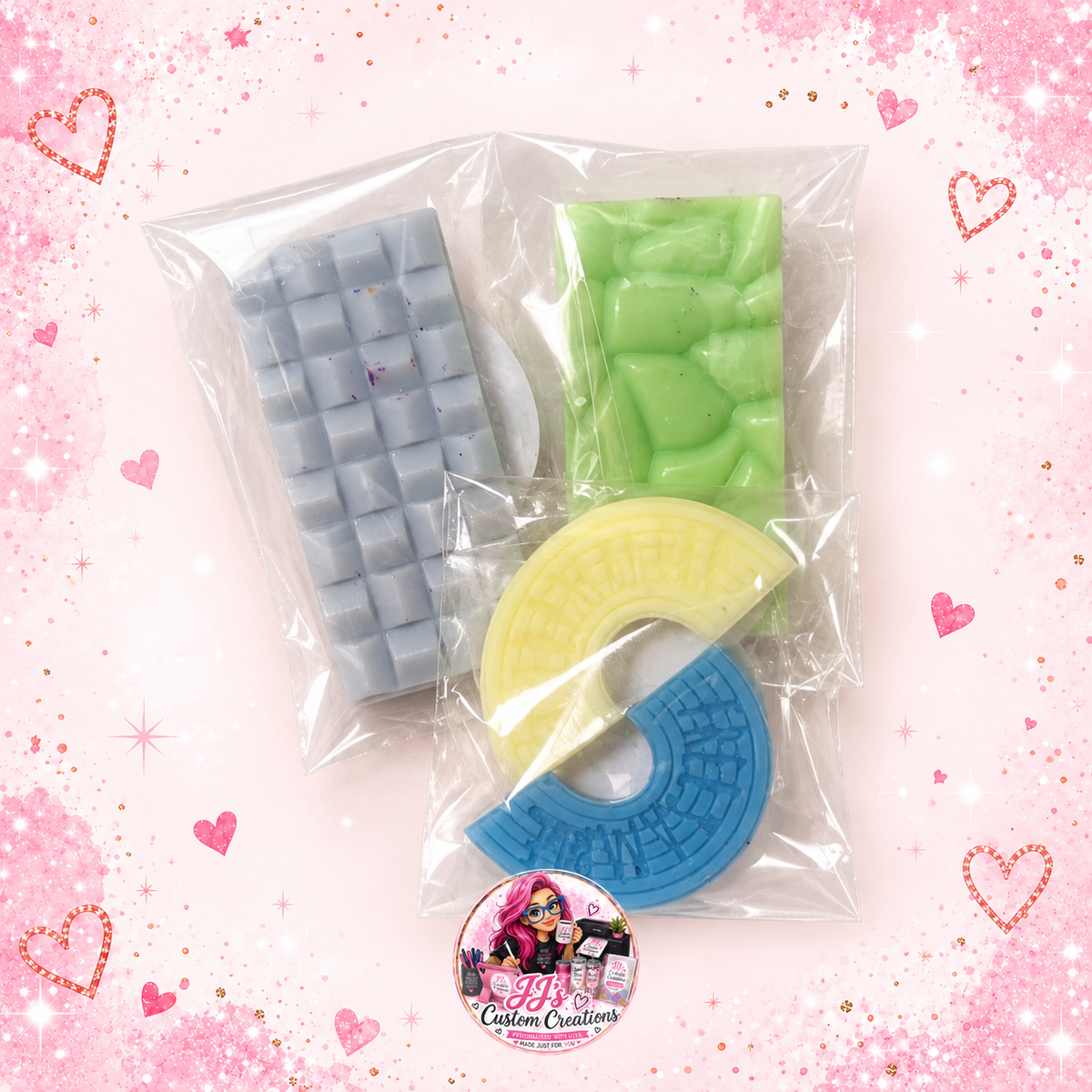 Small bars and shaped wax melts in clear bags on a pale pink sparkle background with JJ's watermark