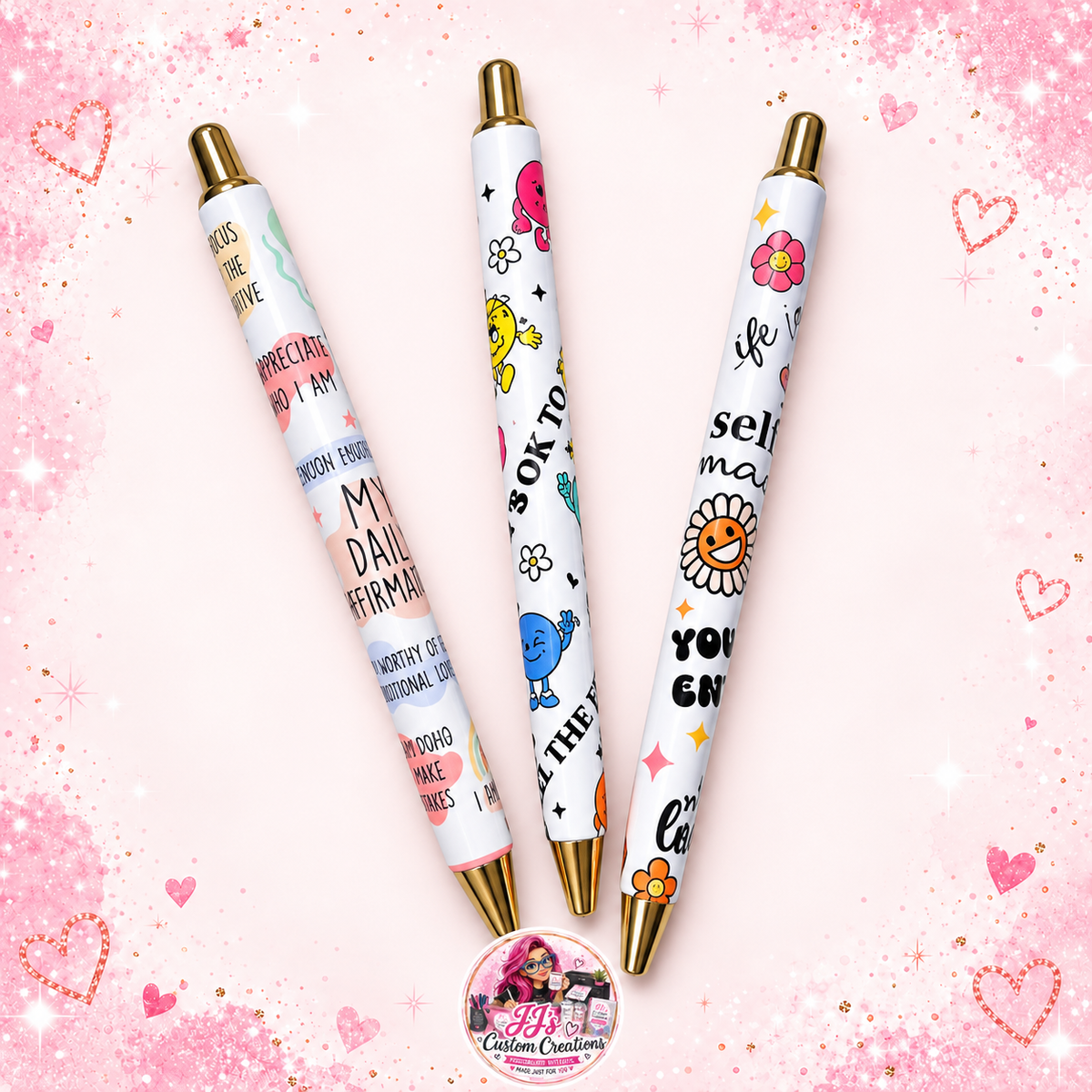 Three affirmation pens with gold details on a pale pink sparkle background with JJ's watermark