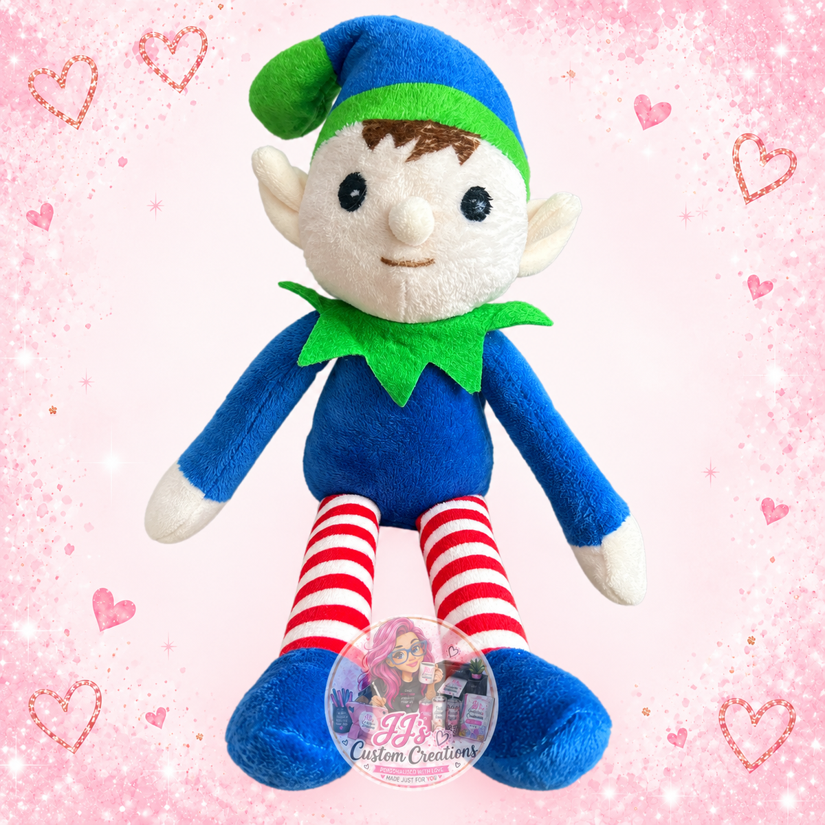 Blue and green plush elf with red striped legs on JJ’s blush pink sparkle background