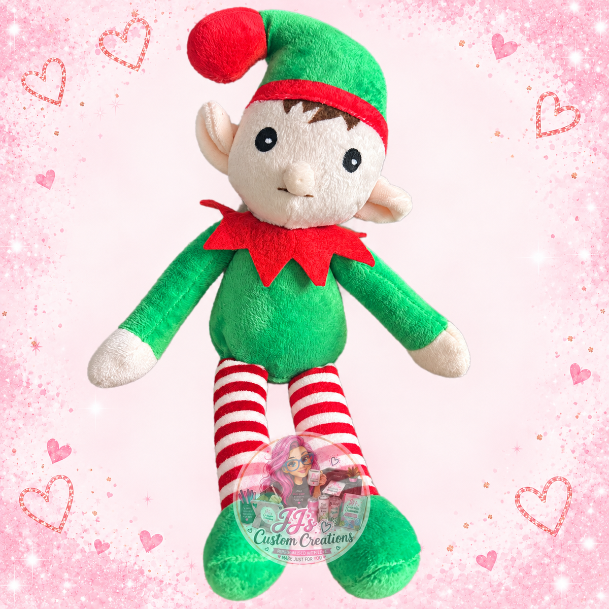 Green and red plush elf with red striped legs on JJ’s blush pink sparkle background