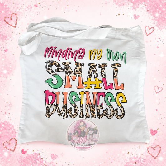 Minding My Own Small Business white tote bag on pale pink sparkle background with JJ's watermark